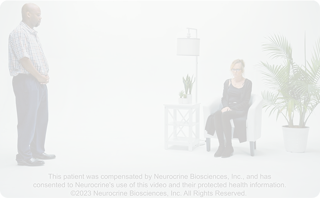A patient sits across a doctor to be evaluated for symptoms using the Abnormal Involuntary Movement Scale (AIMS)